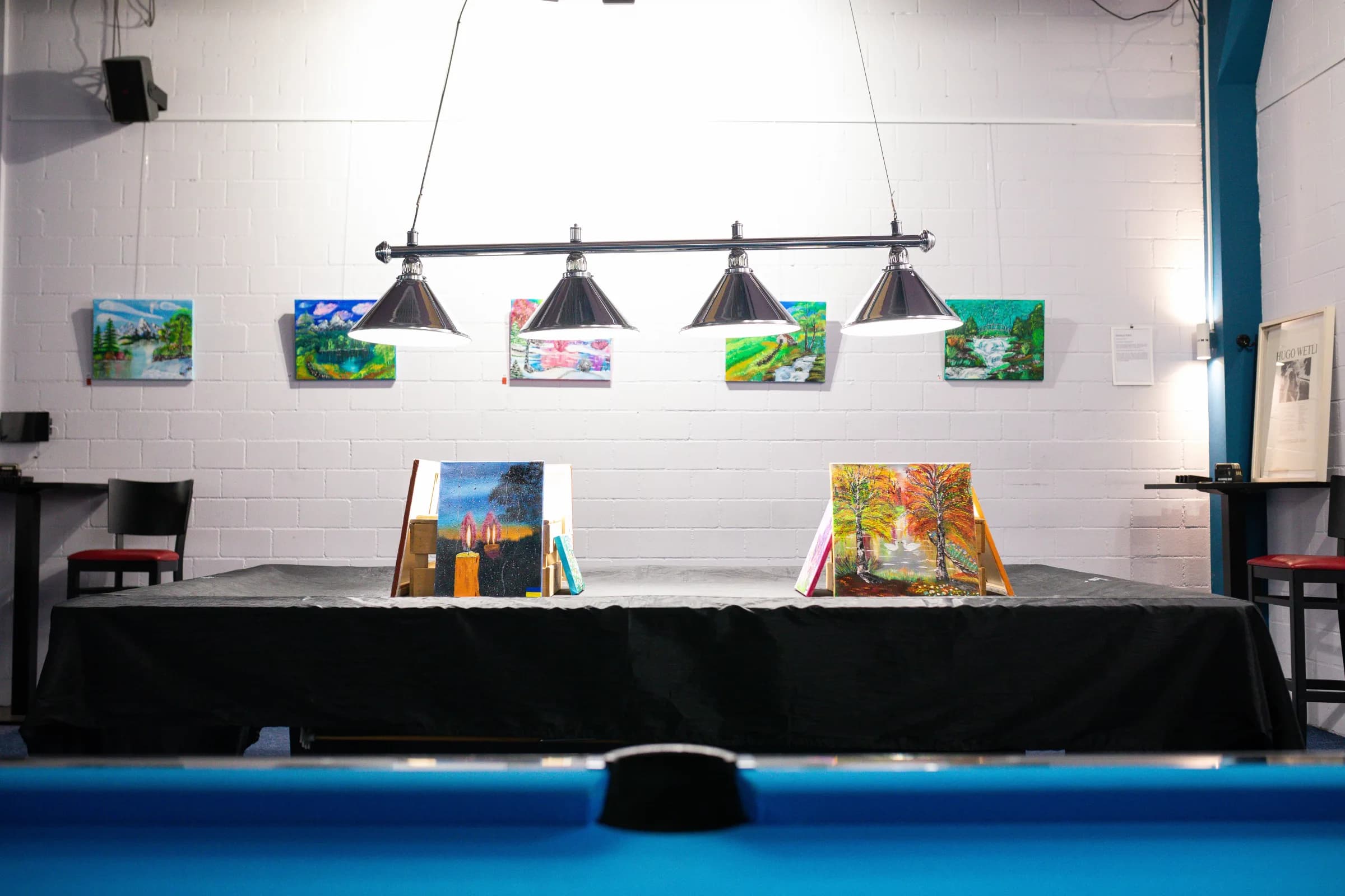 Kunstausstellung im Benteli's – Bilderwand und Leinwände über dem Pooltisch